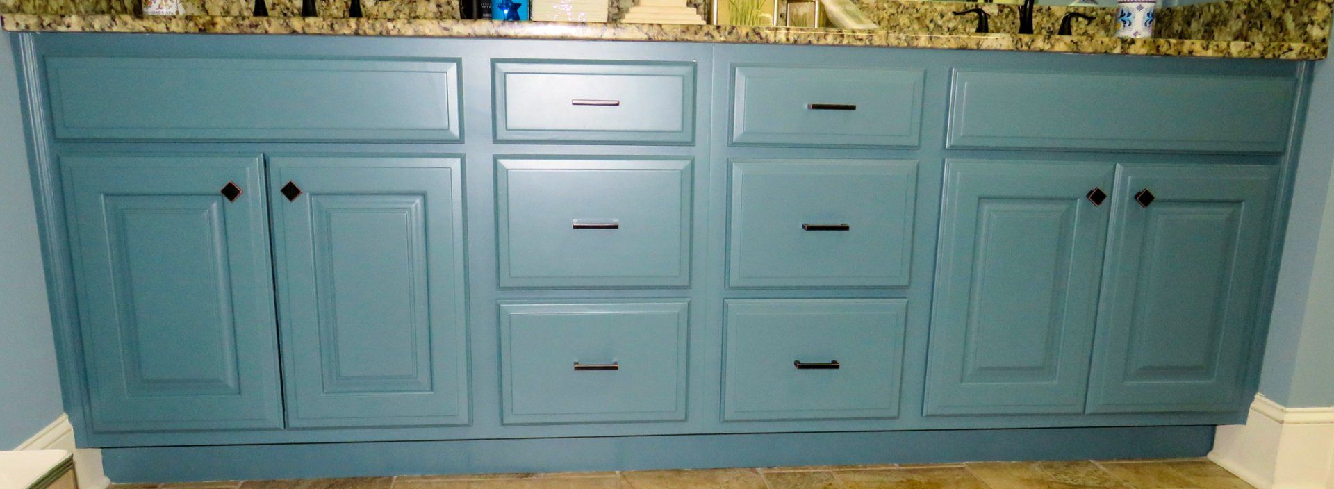 A bathroom vanity with blue cabinets and drawers and a granite counter top.