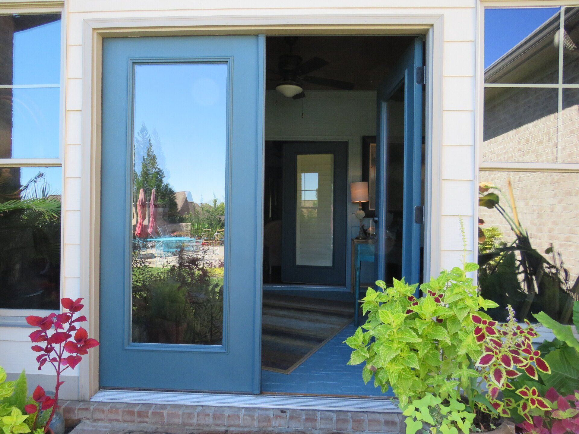 A blue door is open to a house with a lot of windows