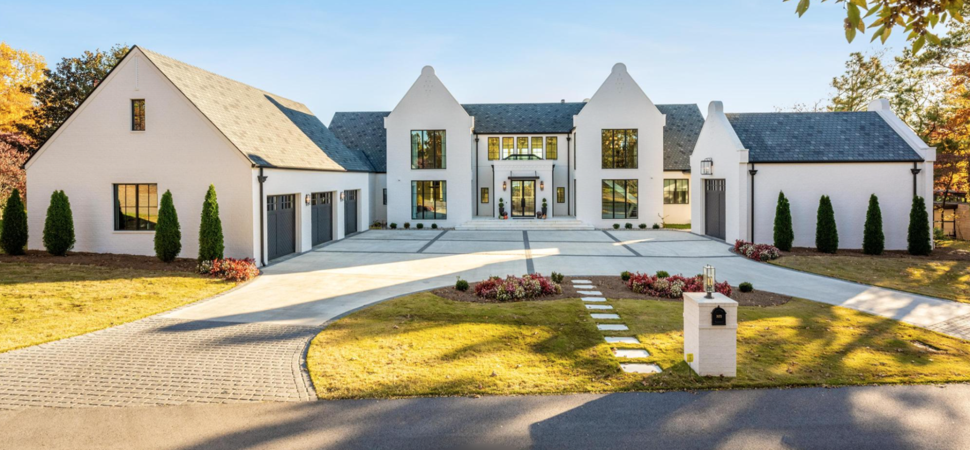 A large white house with a driveway and trees in front of it.