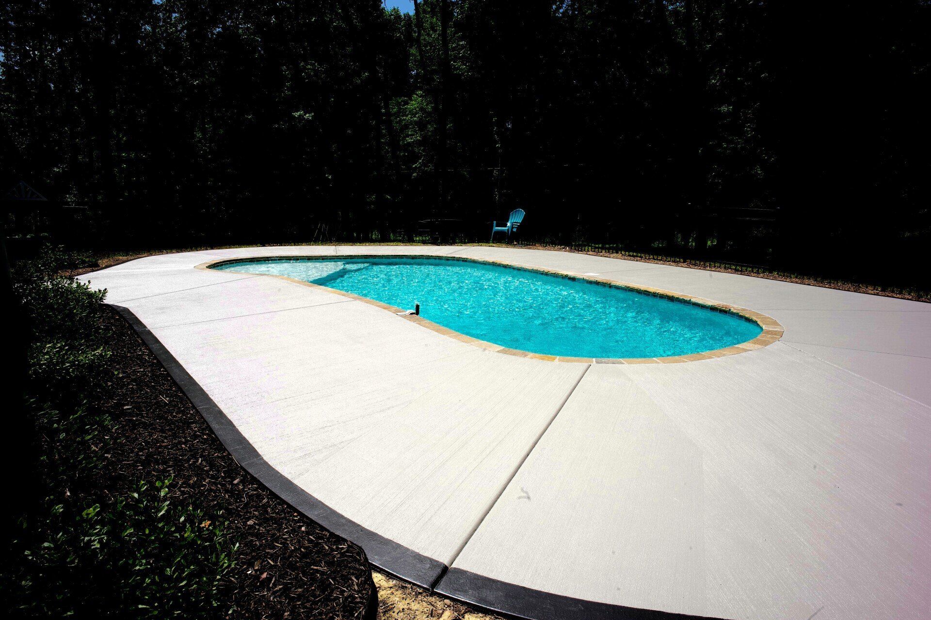 A large swimming pool is surrounded by a white concrete deck