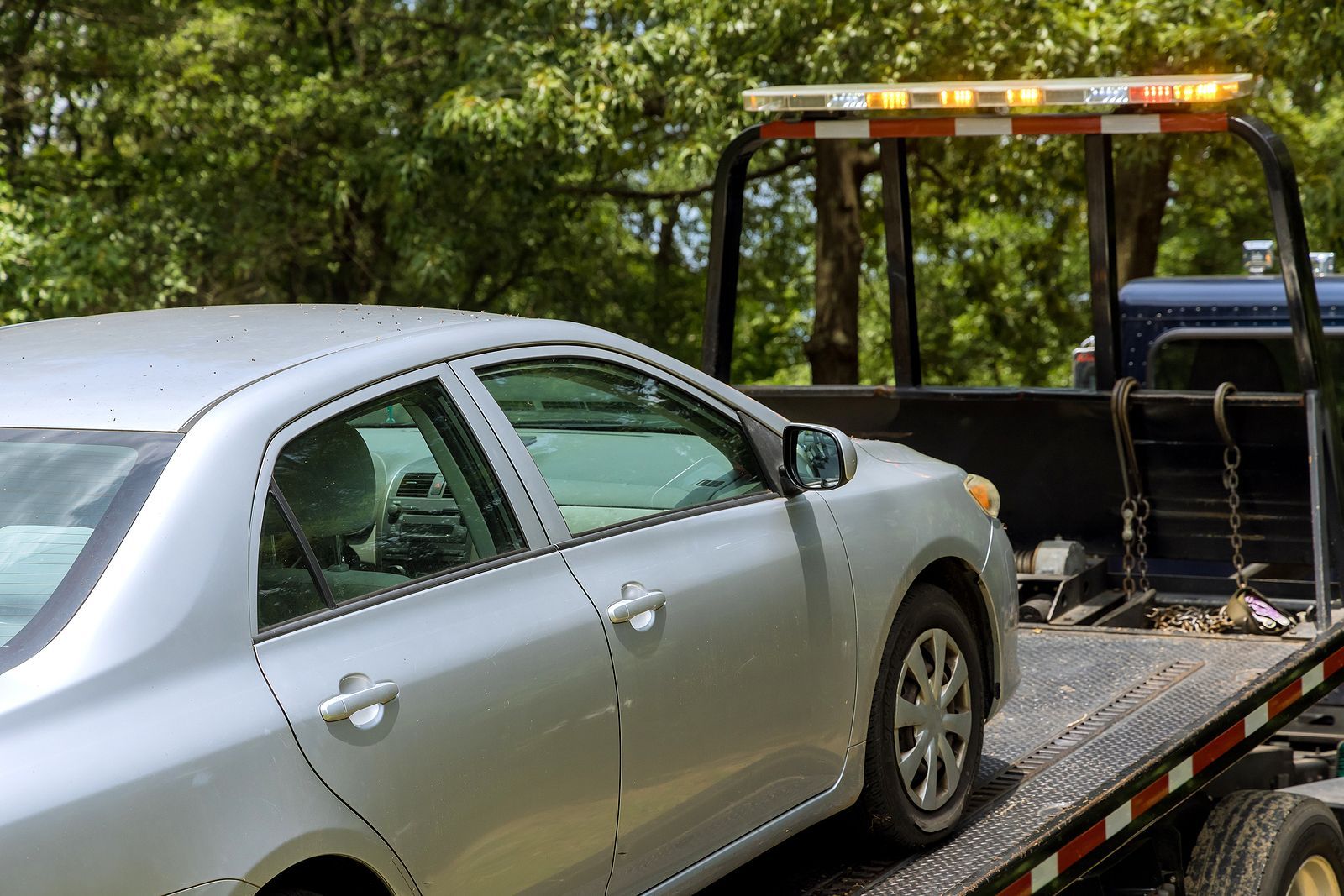 A silver car is sitting on top of a tow truck.