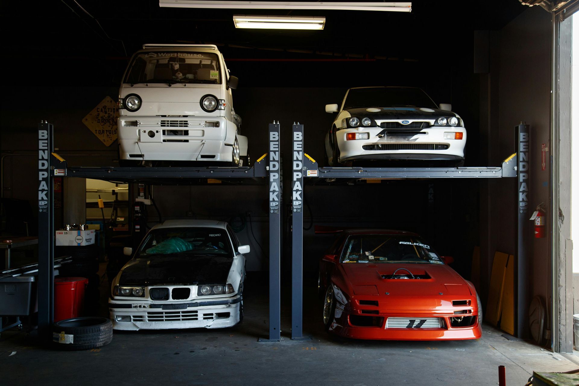 Three cars are parked on a lift in a garage