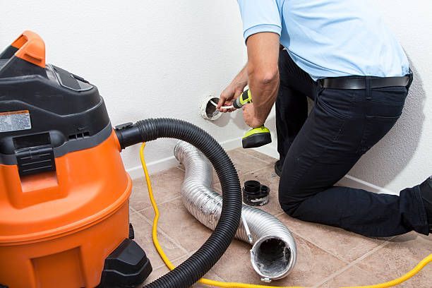 Person using a drill to install a dryer vent with a shop vac nearby.