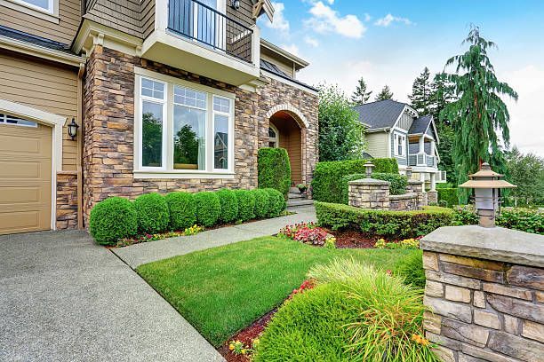 A two-story house with stone facade, manicured lawn, and garden with a blue sky.