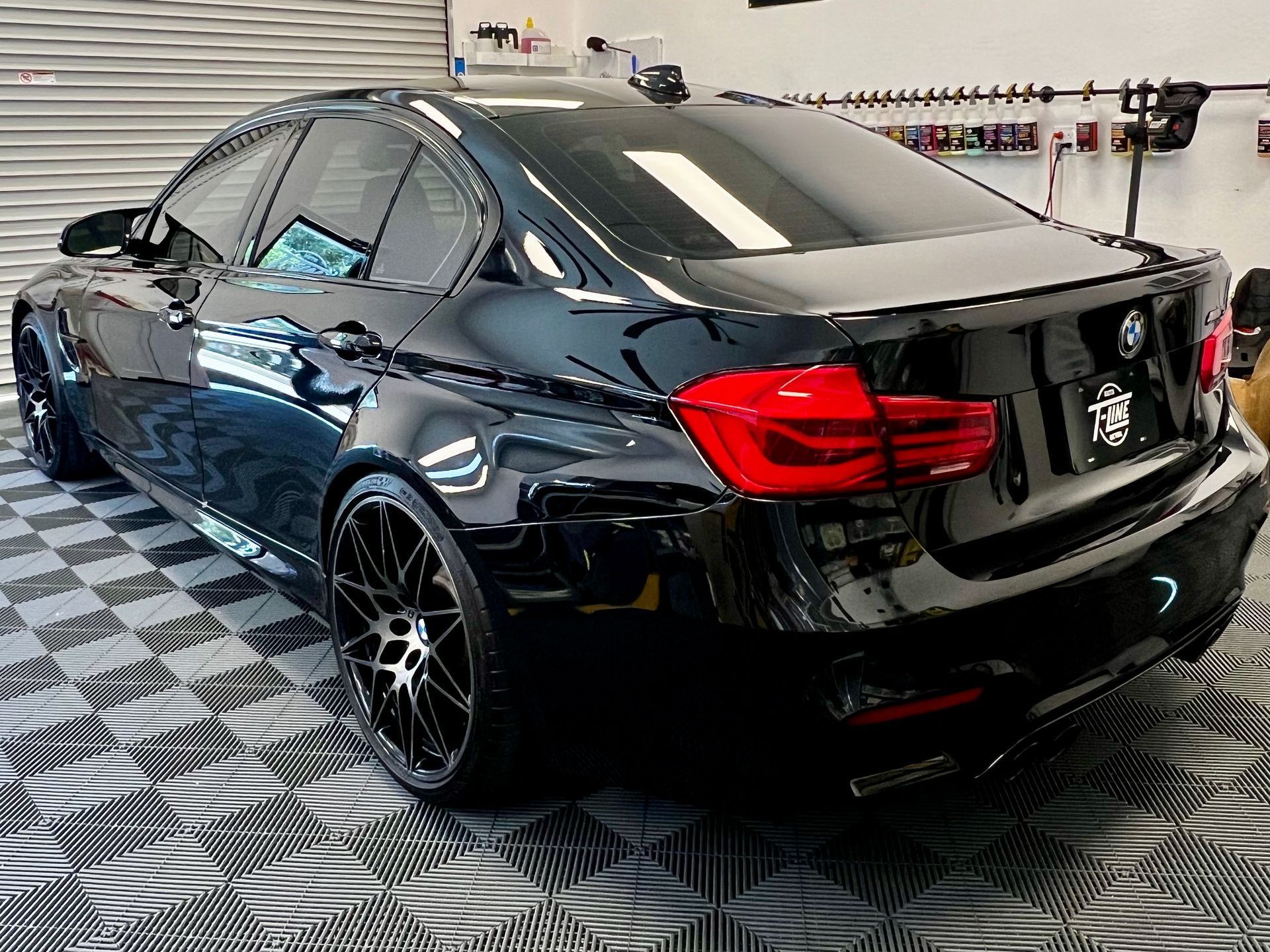 A black bmw m3 is parked in a garage on a checkered floor.