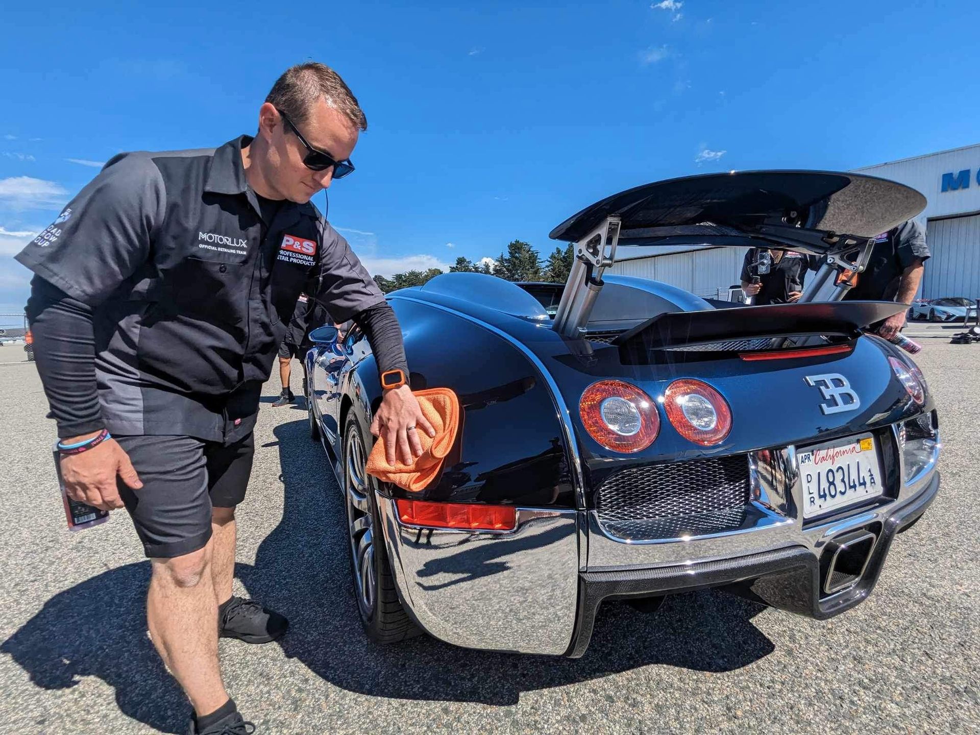 A man is standing next to a bugatti veyron in a parking lot.