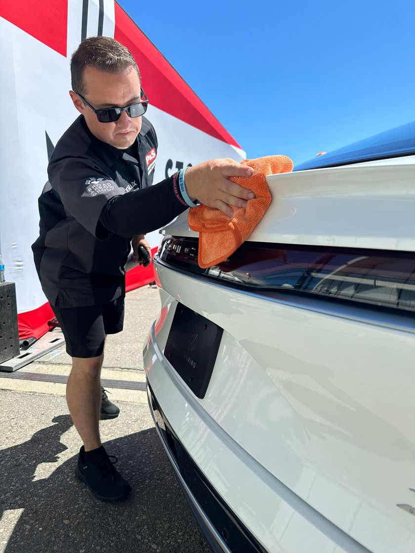 A man is cleaning a white car with a cloth.