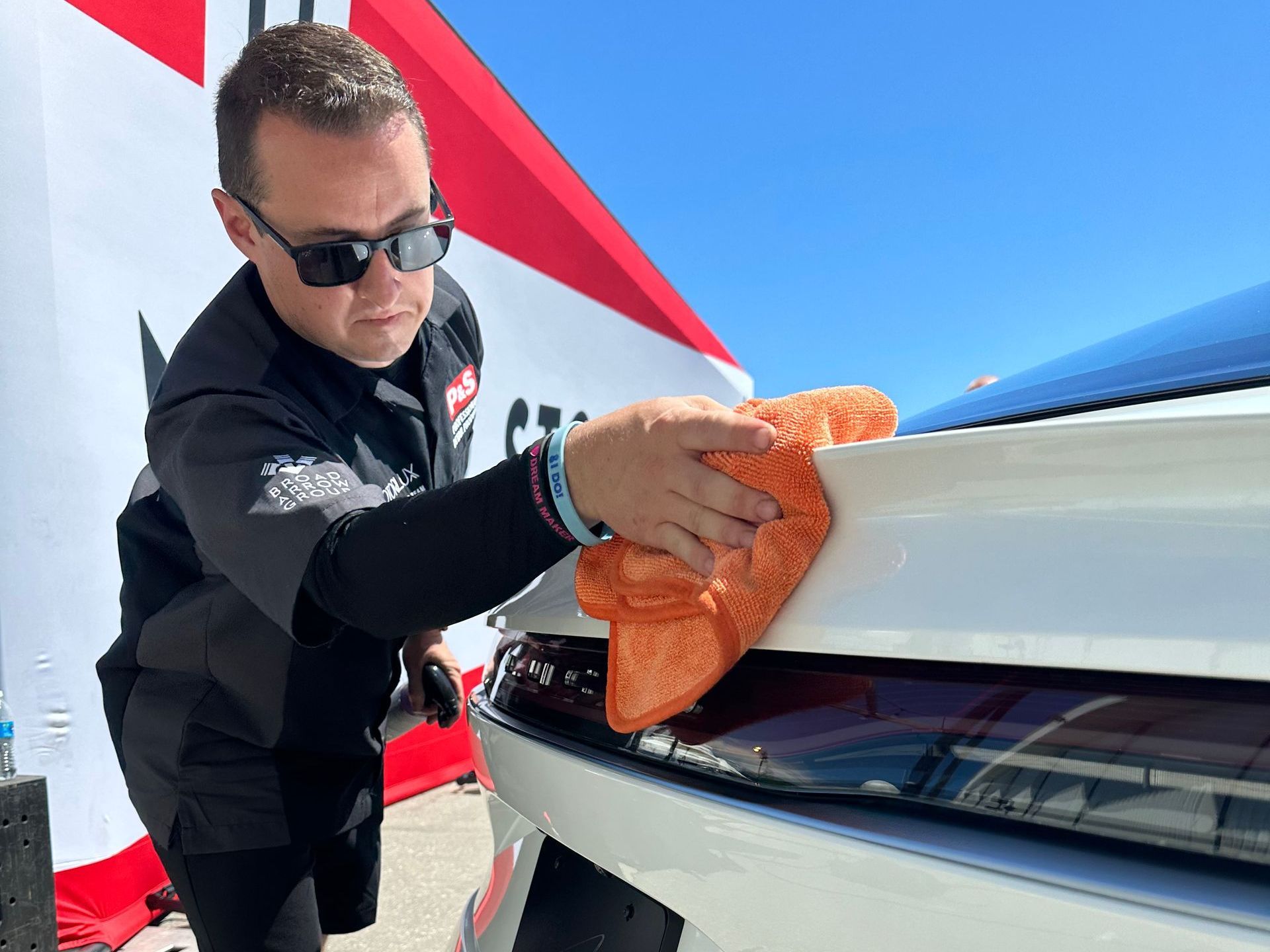 A man is cleaning the front of a white car with an orange cloth.