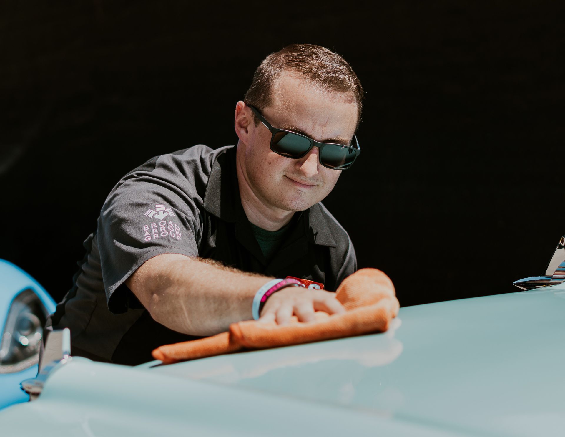 A man wearing sunglasses is polishing a car with a cloth.