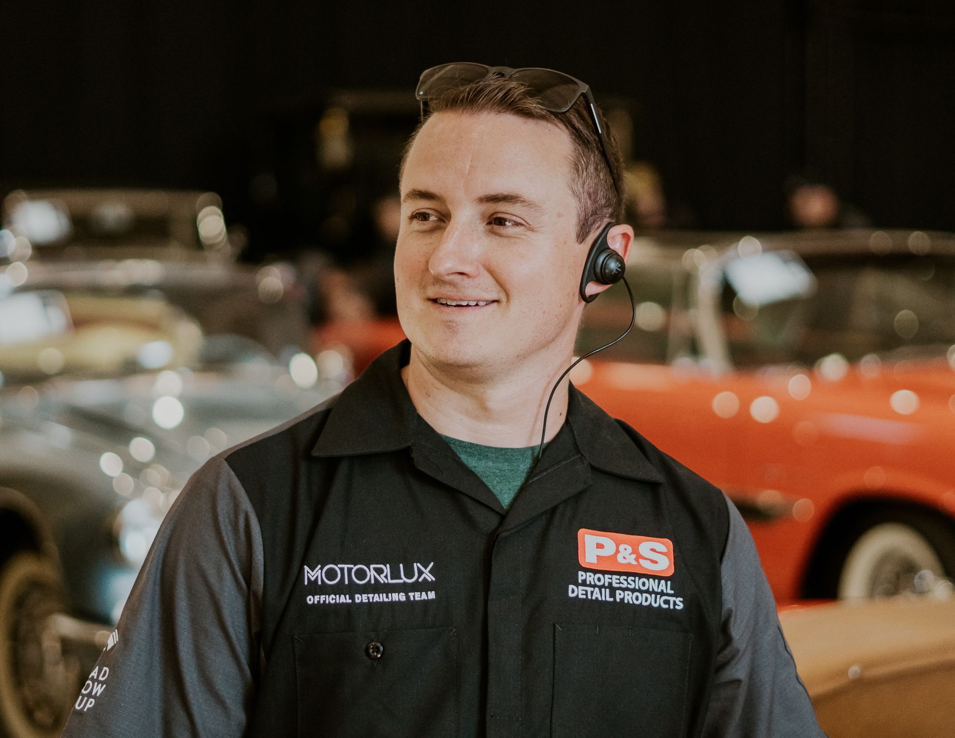 A man wearing a headset is standing in front of a row of cars.