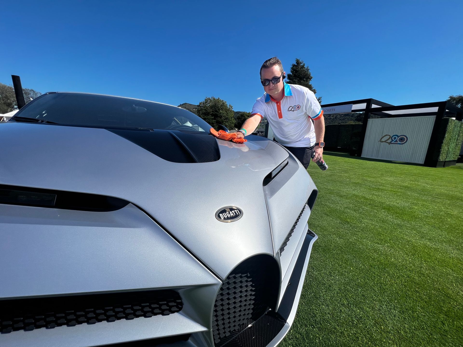 A man is standing next to a silver sports car on a lush green field.