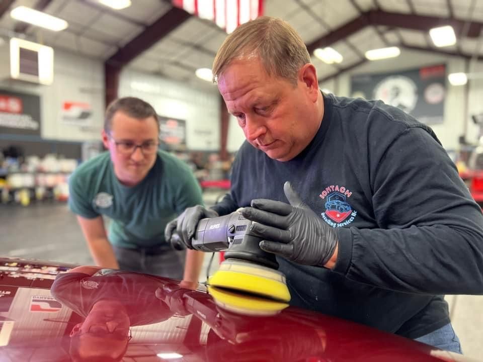 Two men are polishing a red car in a garage.