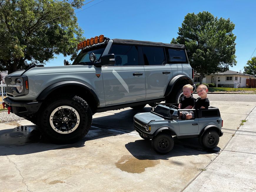 Two children are sitting in a toy bronco next to a ford bronco.