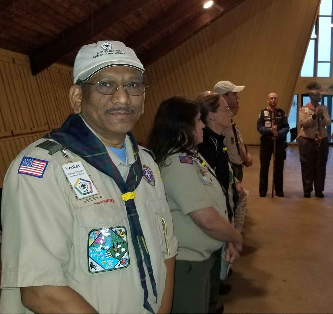 Man in scout uniform smiles at camera, standing with others in a building.