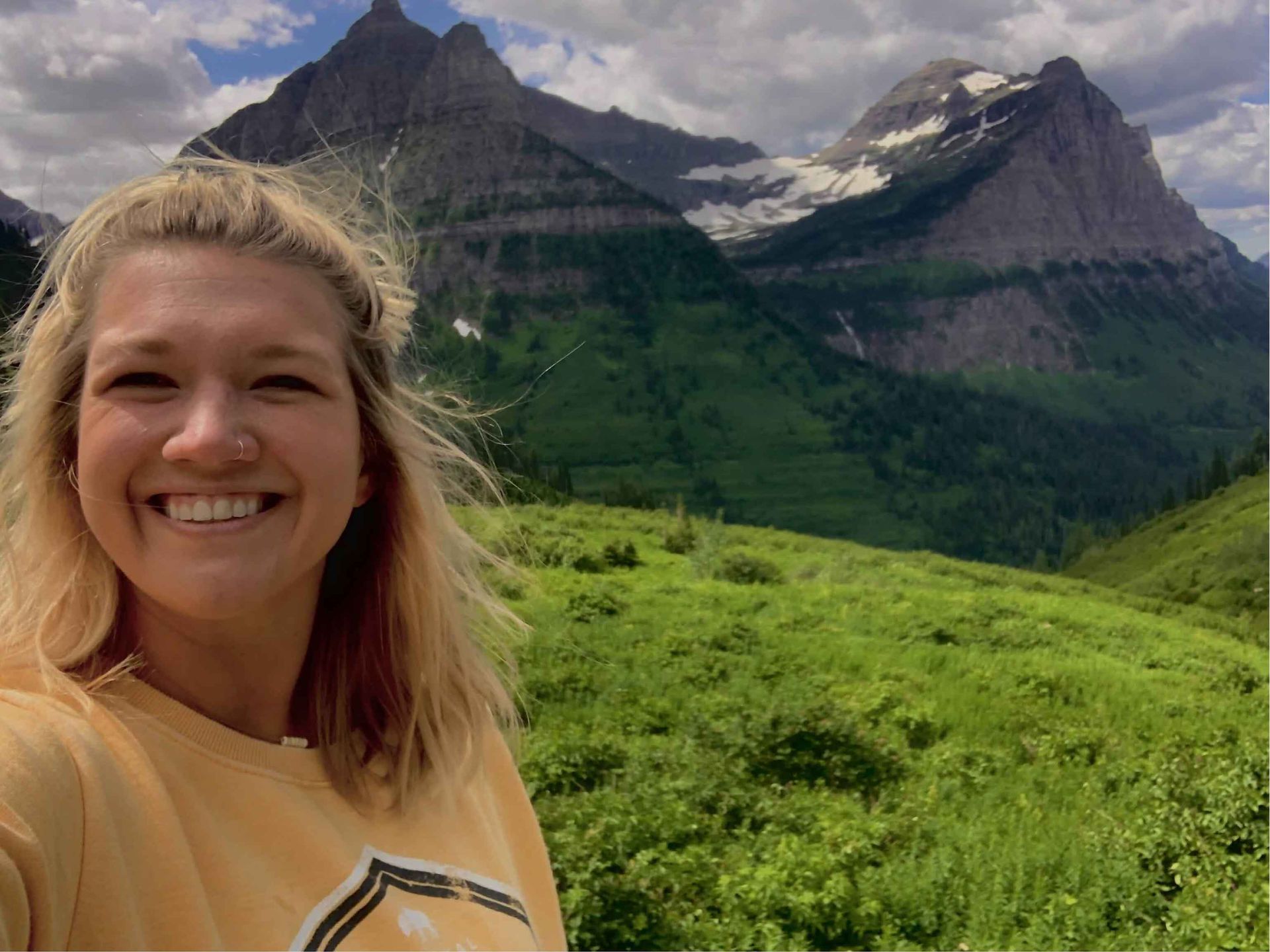 Smiling person in yellow shirt, mountains in background with green valley.