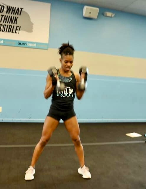 Woman in gym doing dumbbell workout, legs apart, focused expression.