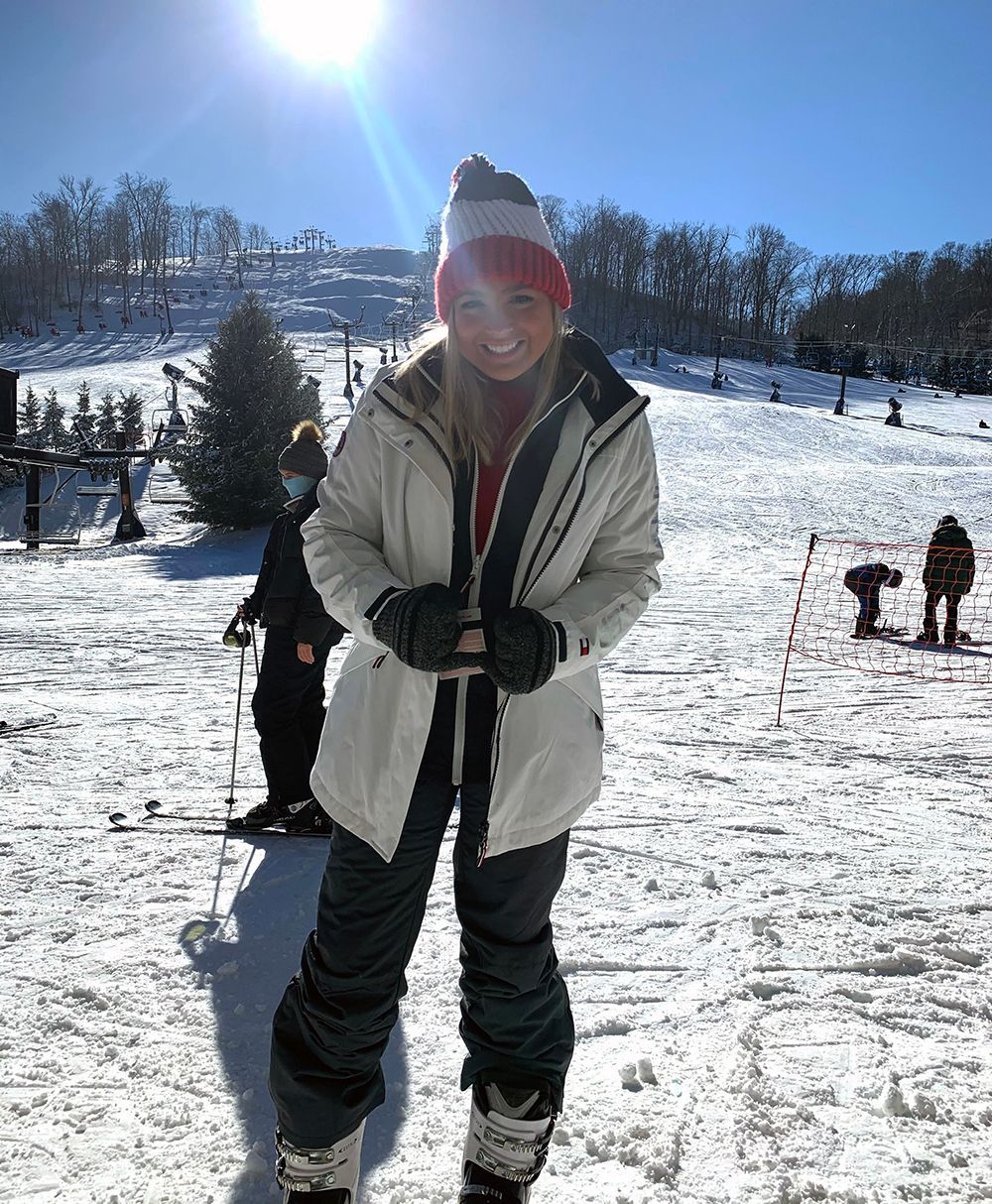 Woman in winter gear smiles on a snowy ski slope. The sun shines brightly.