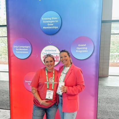 Two women smiling in front of a promotional banner with marketing strategies and club membership information.