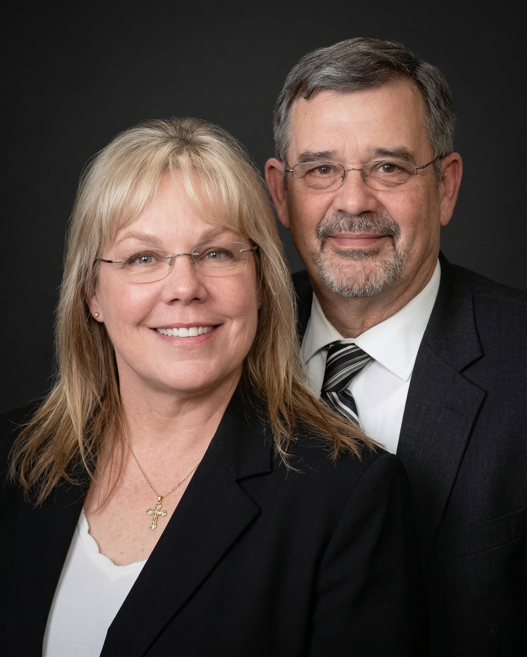 A professional headshot of two smiling individuals posed together against a plain black background.