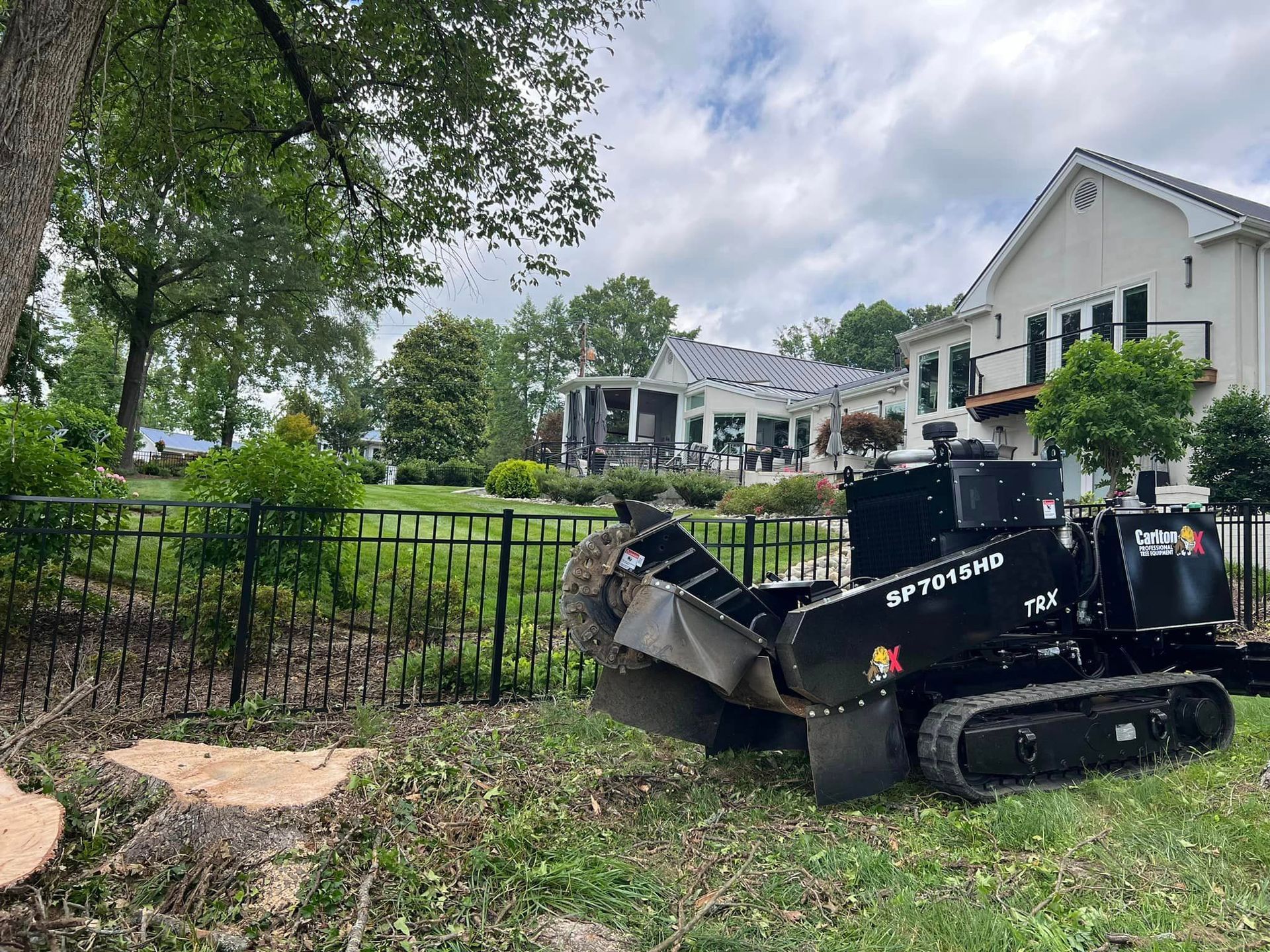 A stump grinder is sitting in the grass in front of a house.
