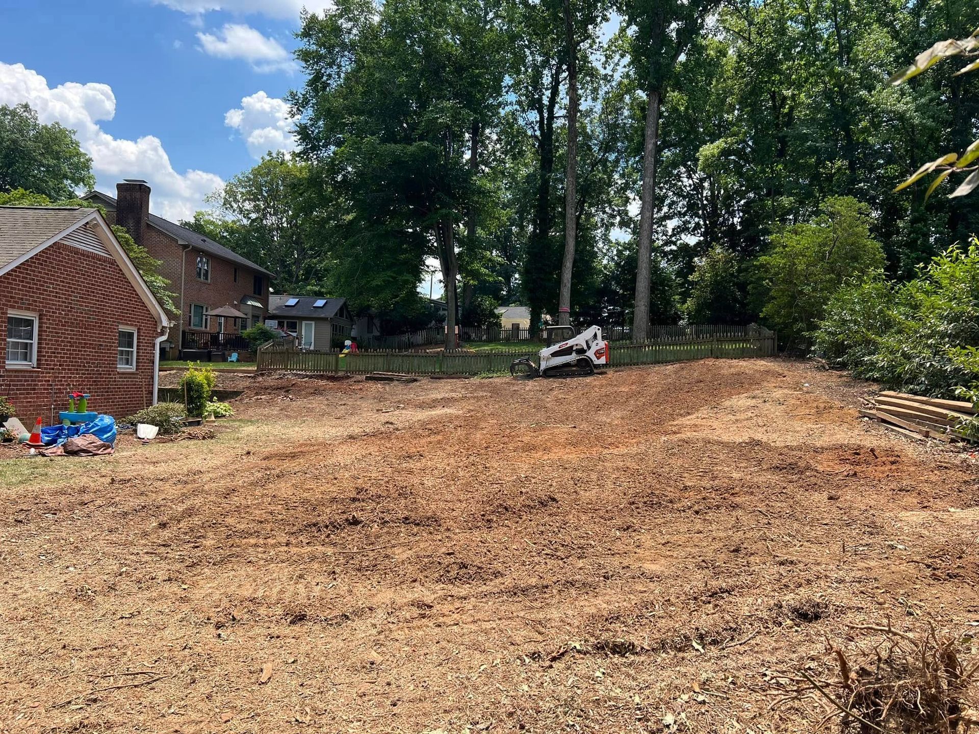 A large dirt field with a house in the background and trees in the background.
