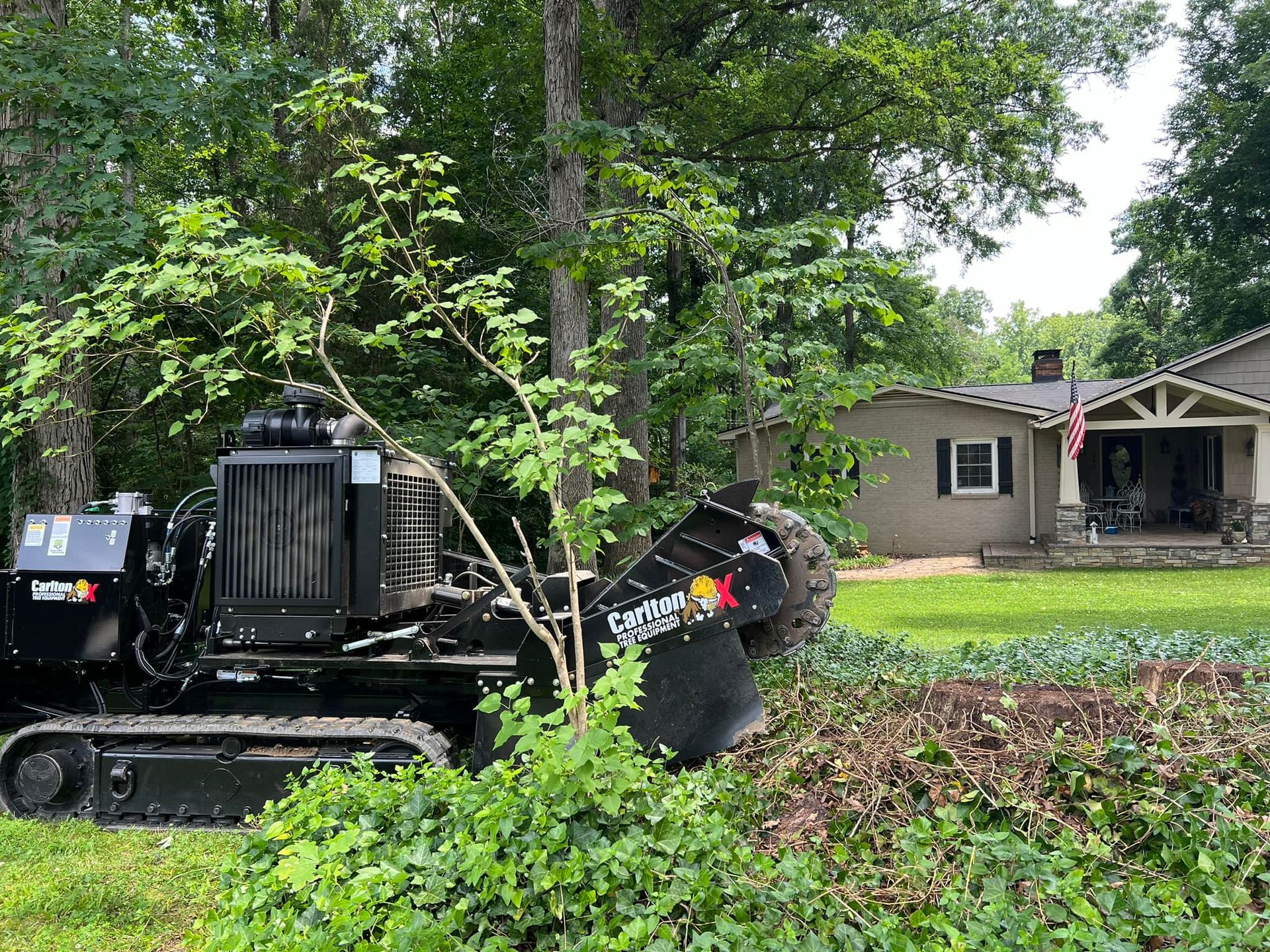A tractor is cutting down a tree in front of a house.