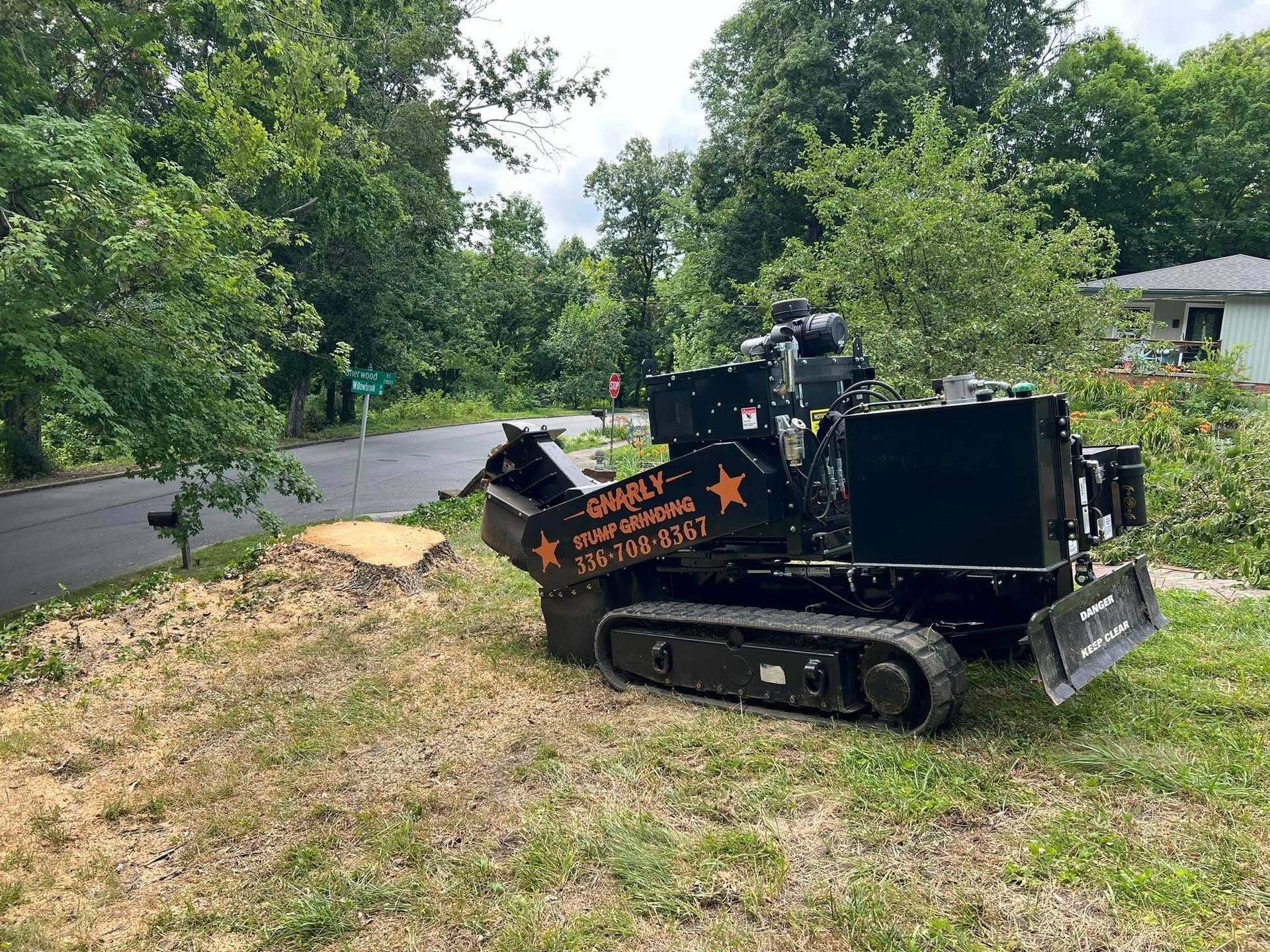 A stump grinder is sitting in the grass next to a tree stump.