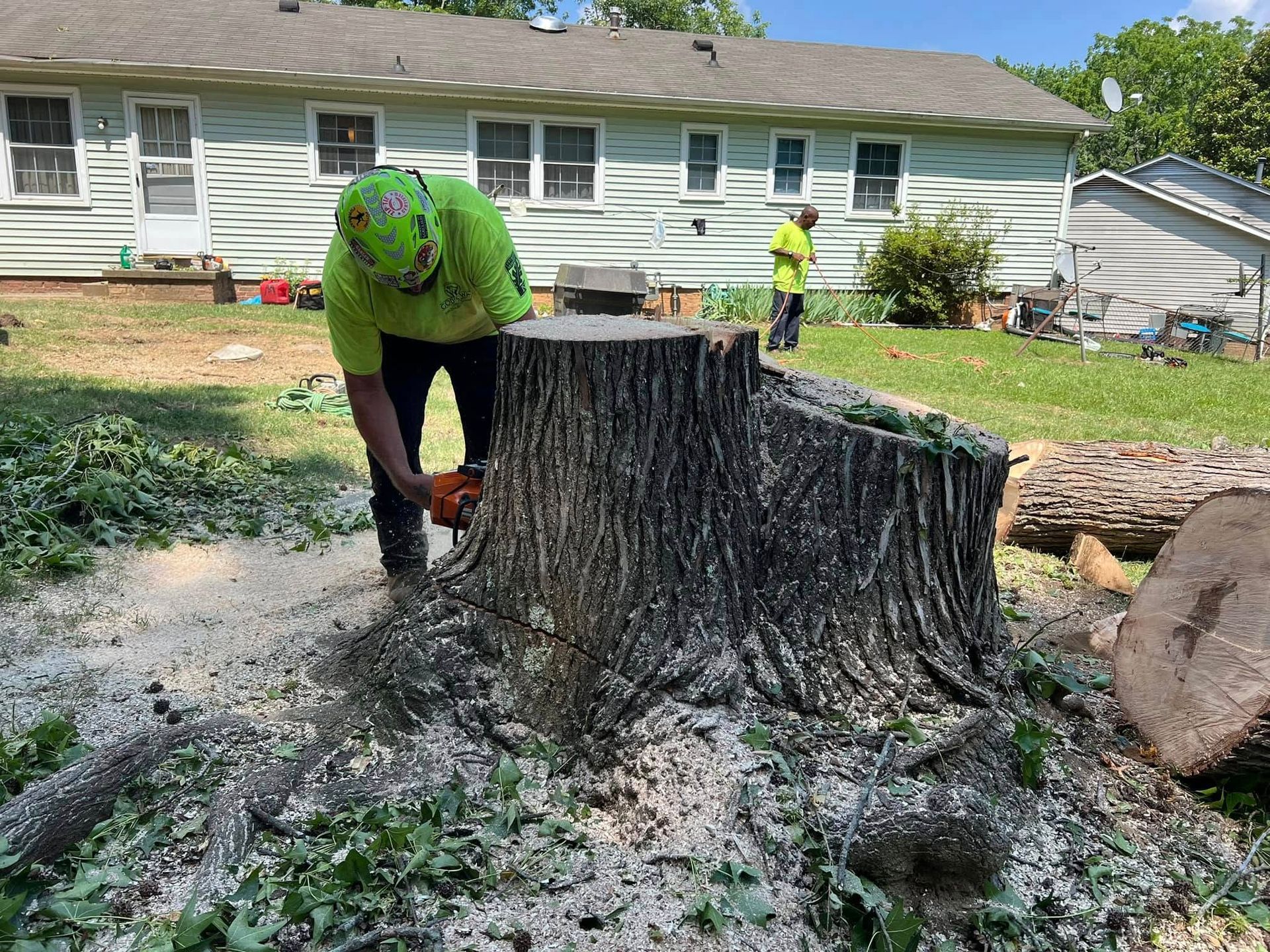 A man is cutting a tree stump with a chainsaw in front of a house.