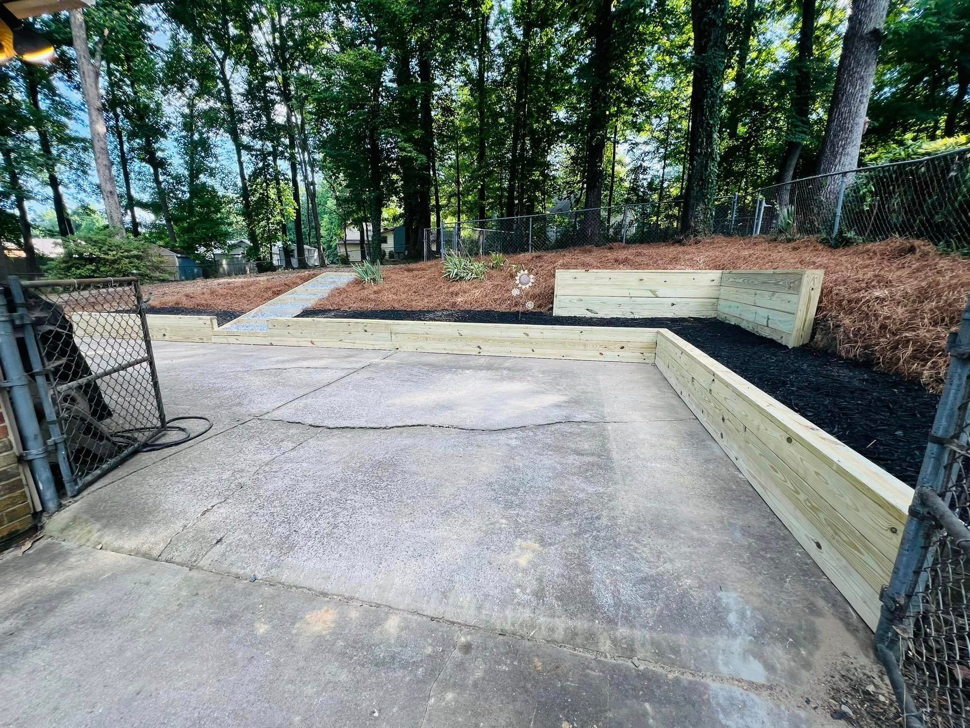 A concrete driveway with a wooden fence and trees in the background.