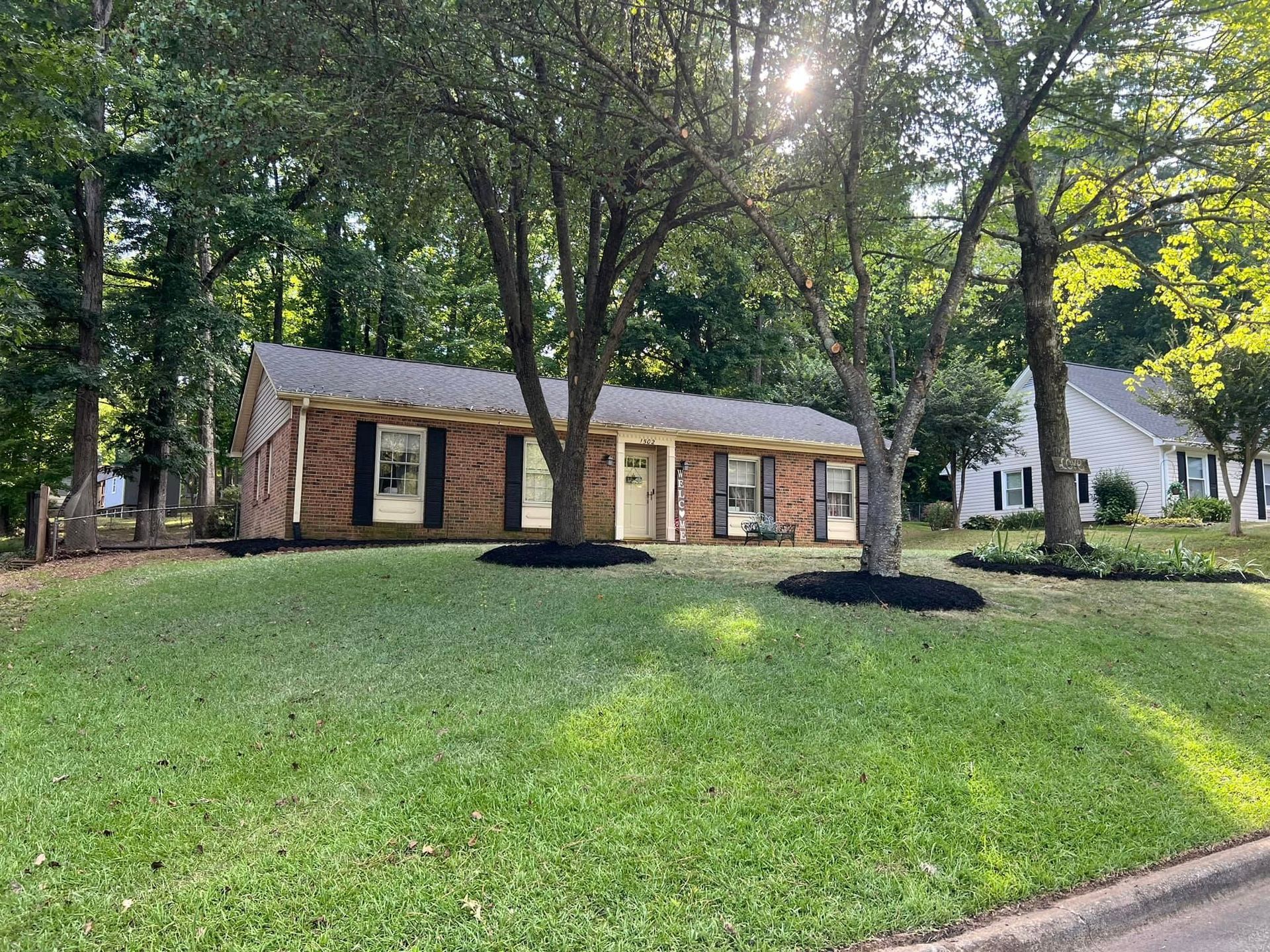 A brick house with a lush green lawn and trees in front of it.