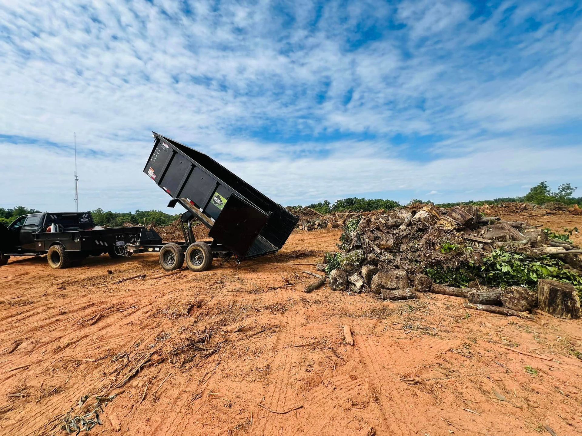 A dump truck is being towed by a trailer in a dirt field.
