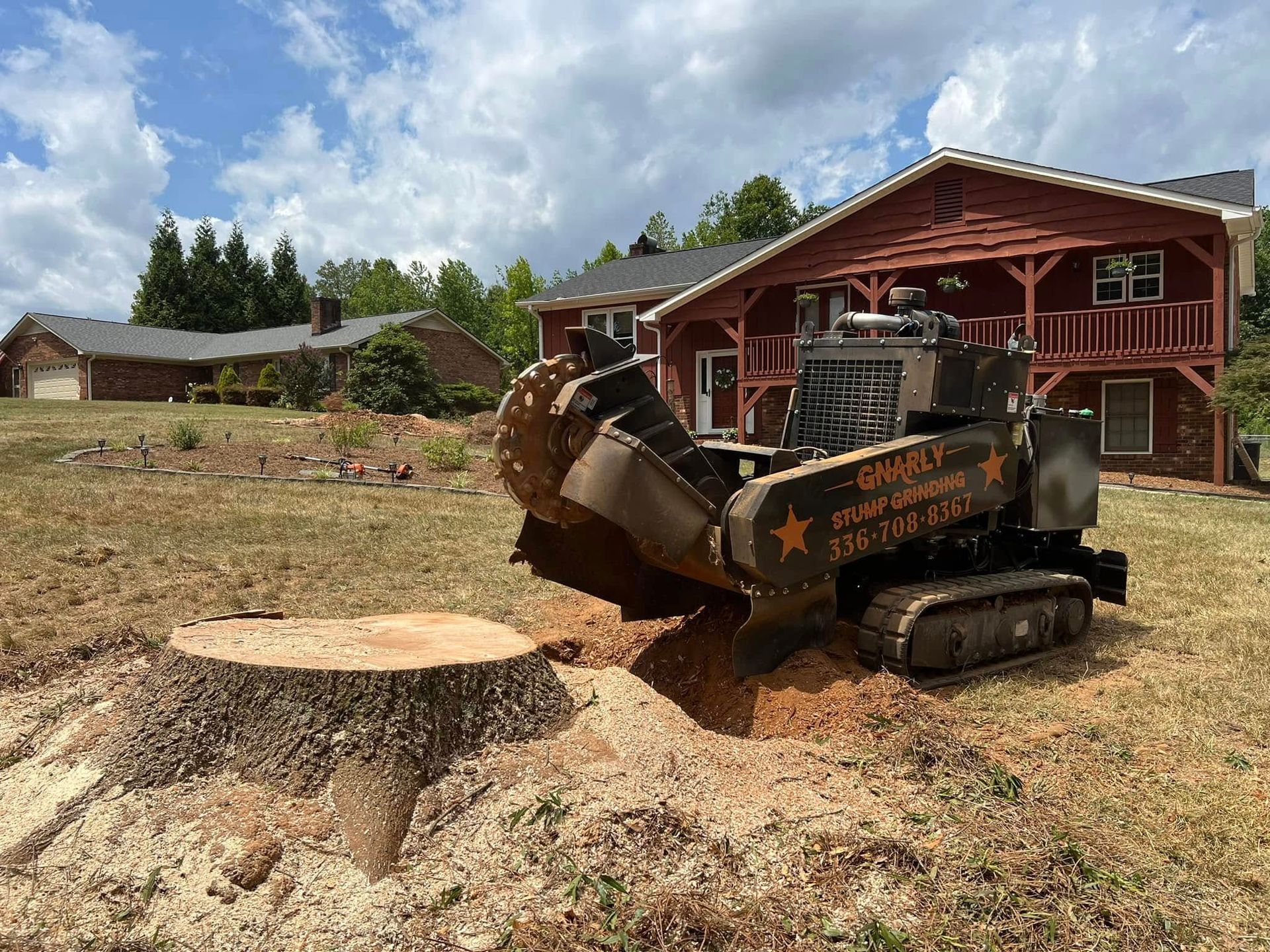 A large tree stump is being removed by a machine in front of a house.