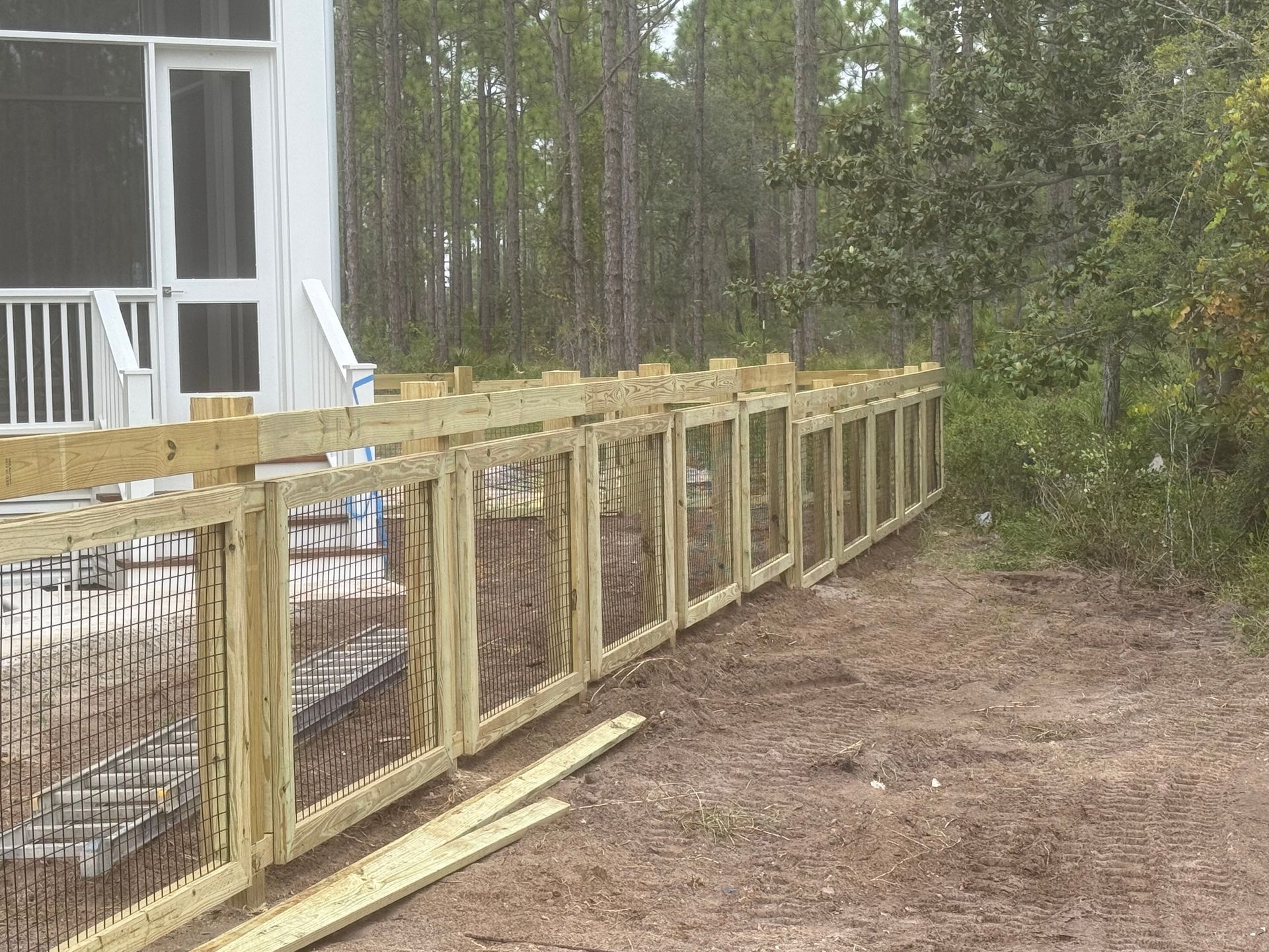 Wooden fence with black decorative inserts, next to a house in a wooded area.