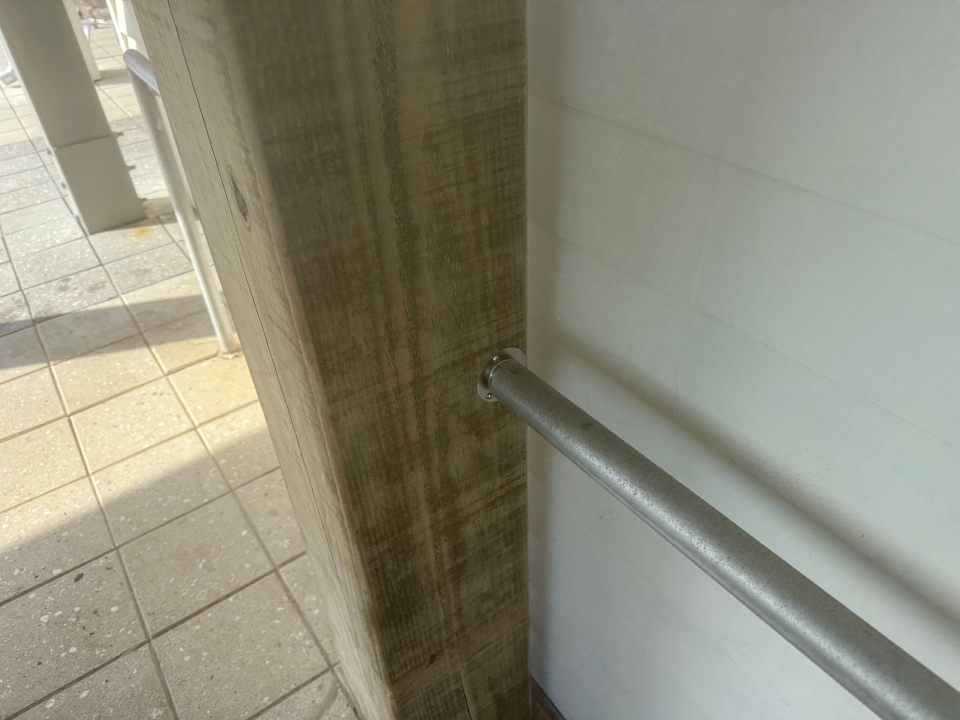 Gray metal handrail extending from a white wall into a textured column. Paved ground in the background.