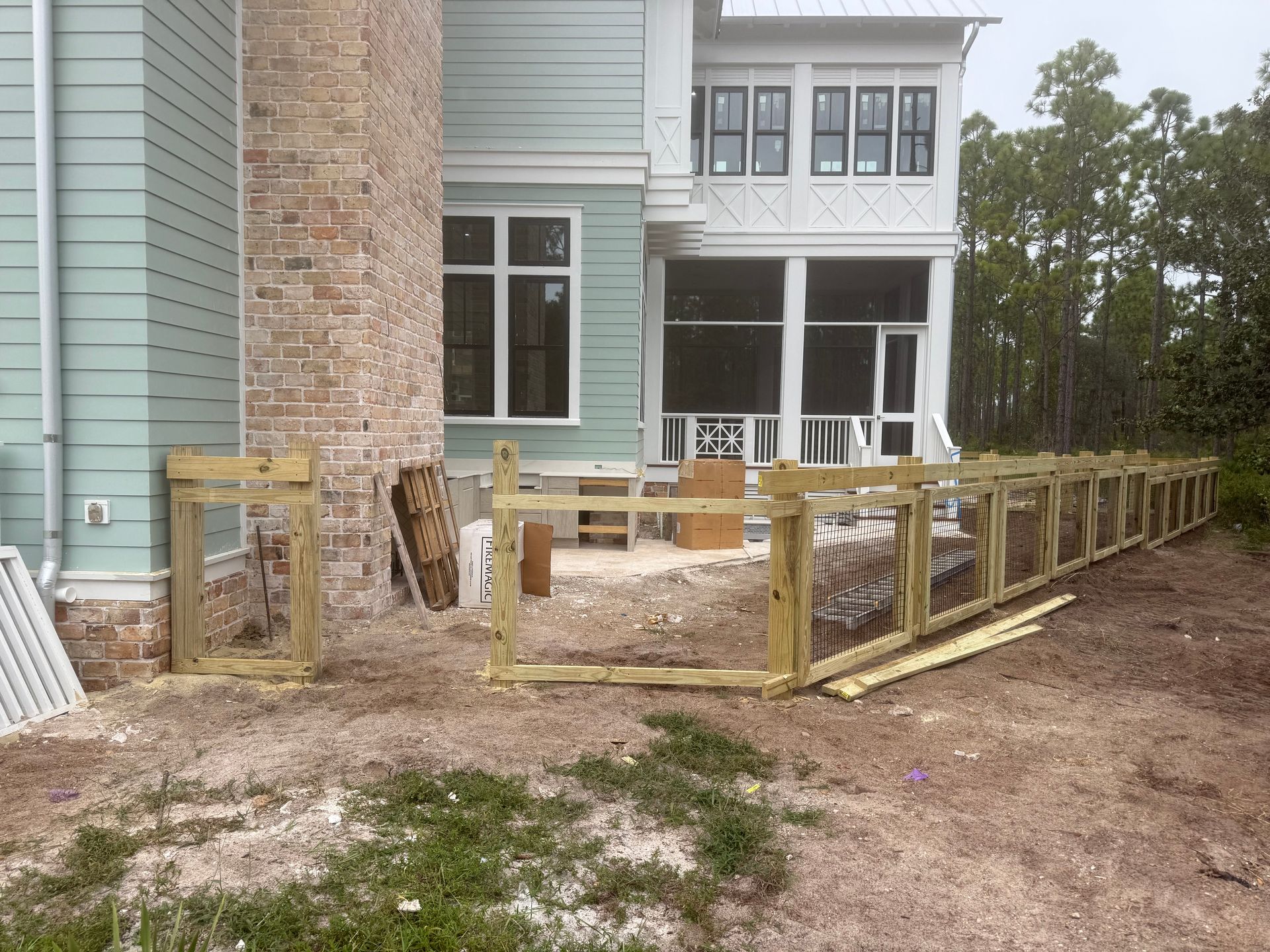Wooden fence under construction outside a two-story house with a brick chimney.