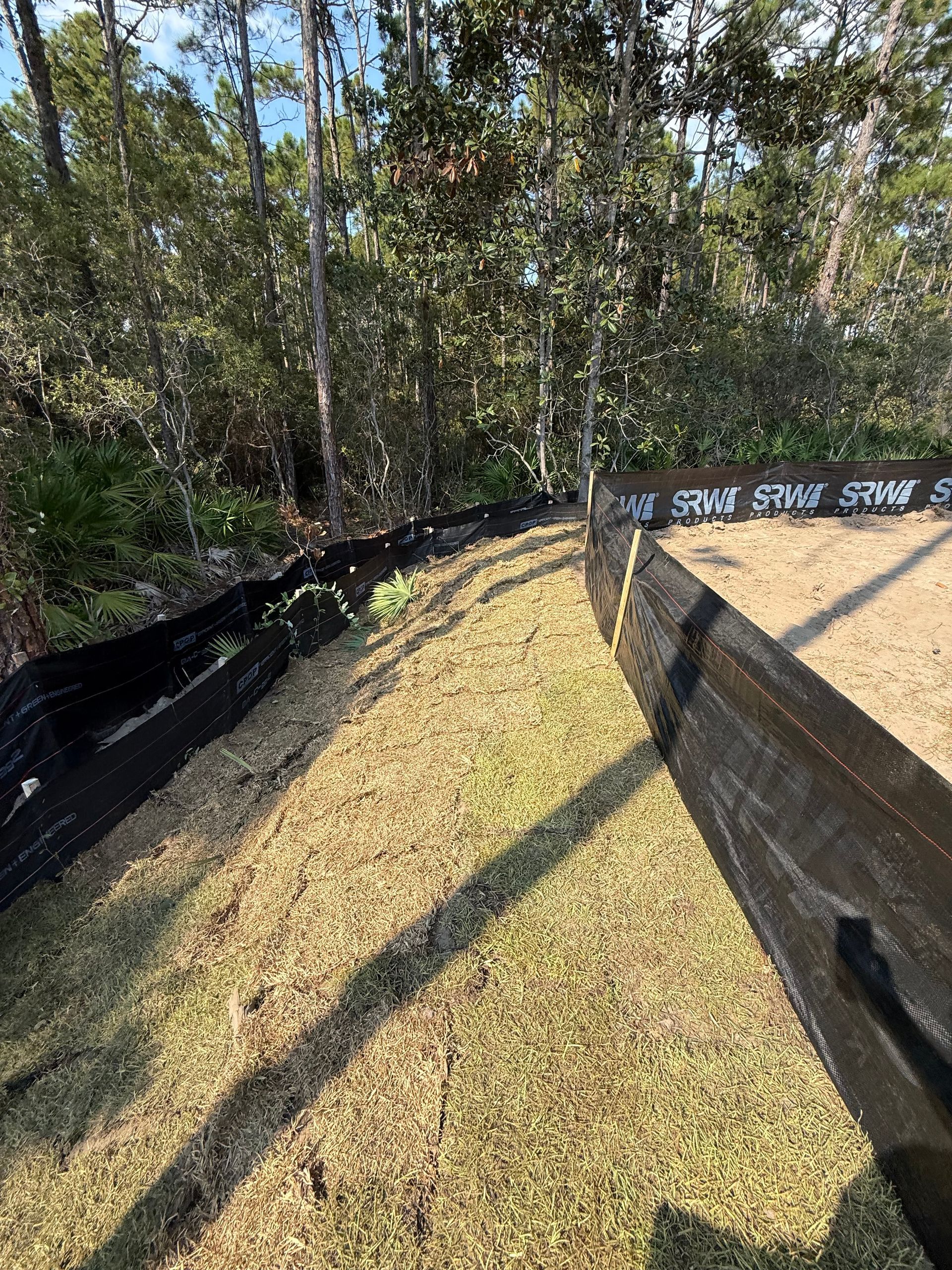 Erosion control barriers lining grassy area next to trees. Wooden fence with the word