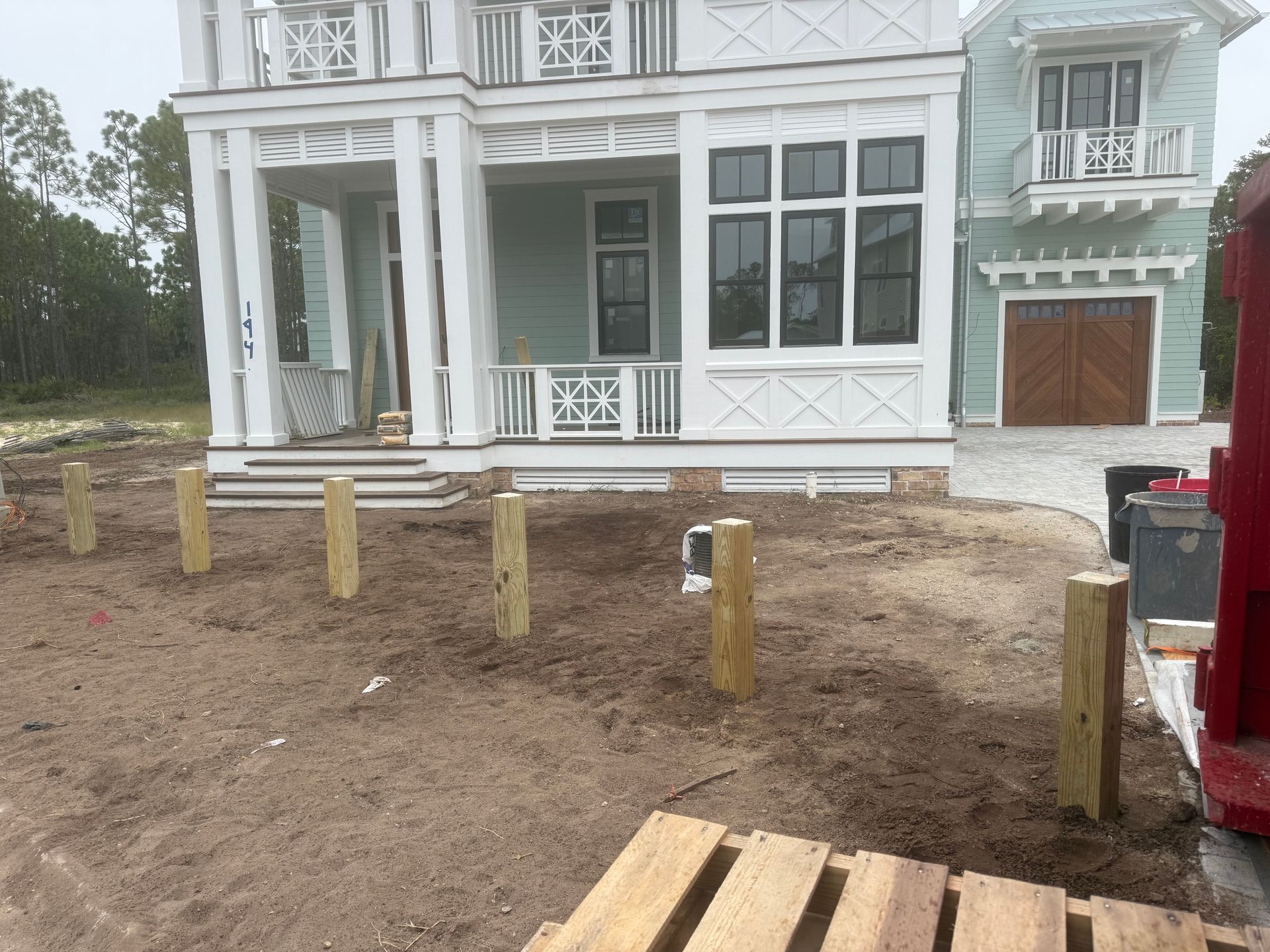 Wooden support posts in muddy ground in front of a light blue house.