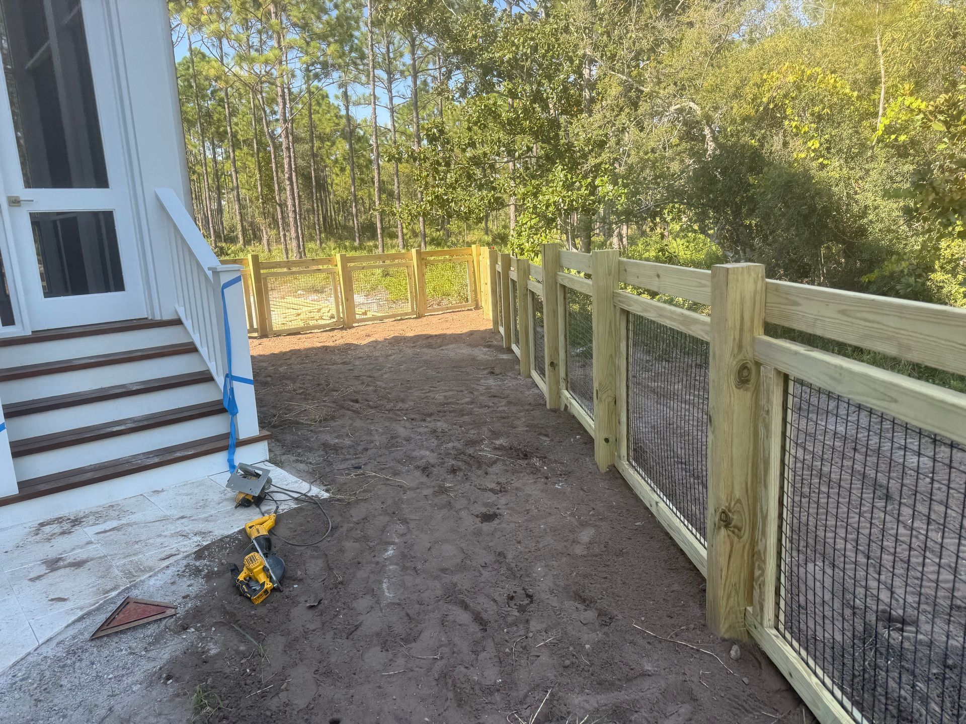 A wooden fence with decorative panels along a dirt path next to a house.
