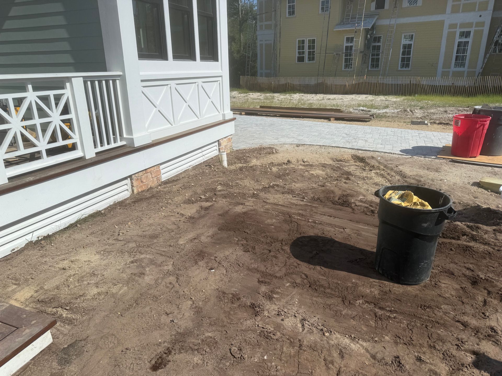 Dirt yard with a porch, trash can, and construction materials.
