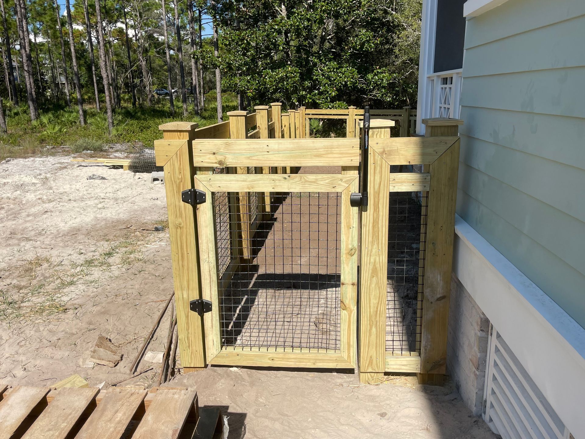Wooden gate with black iron bars, opening to a pathway, next to a pale blue house.