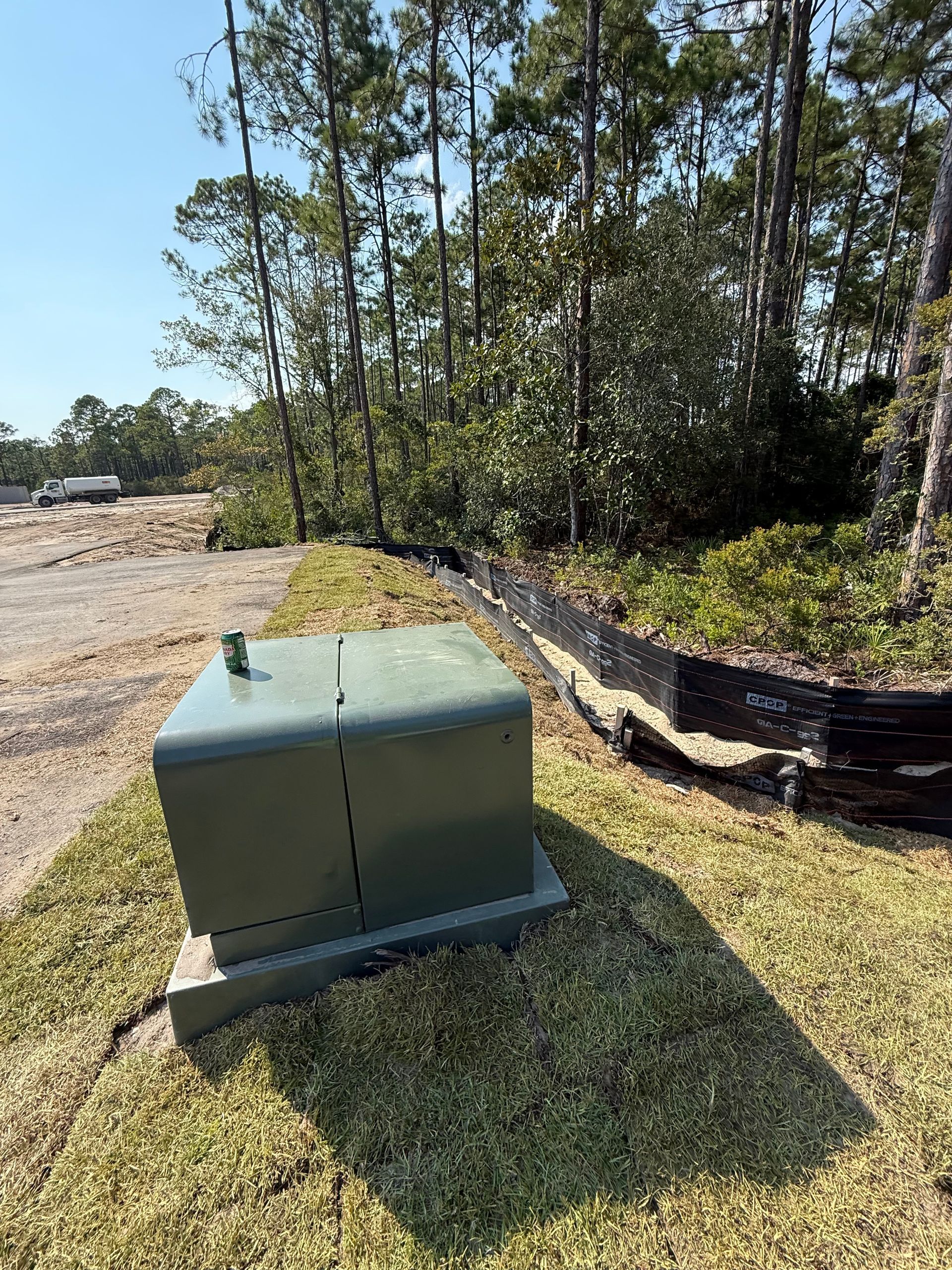Green electrical box on grass, with a treeline in the background, and blue sky.