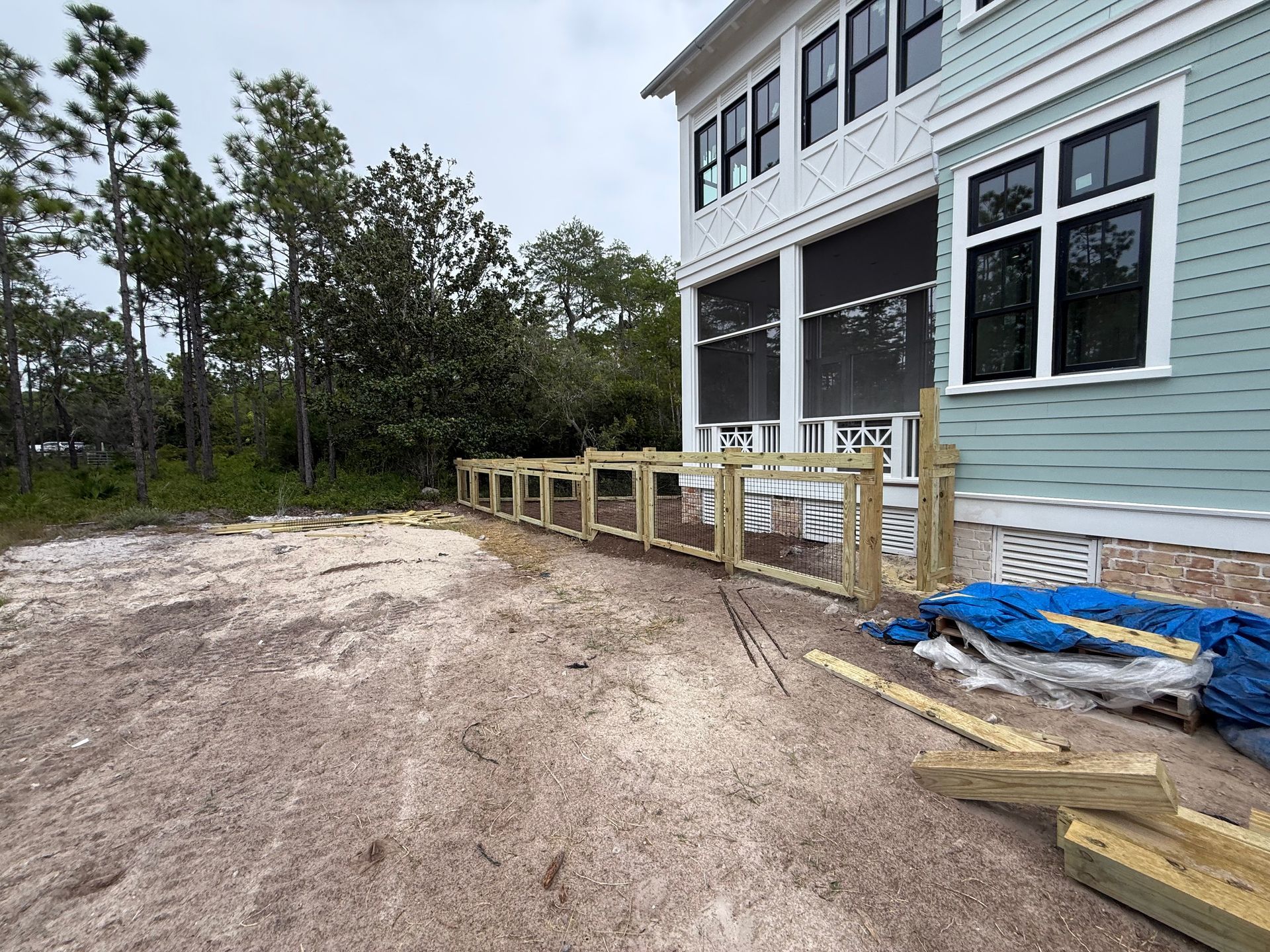 A new wooden fence being built next to a light blue house and a pile of gravel.