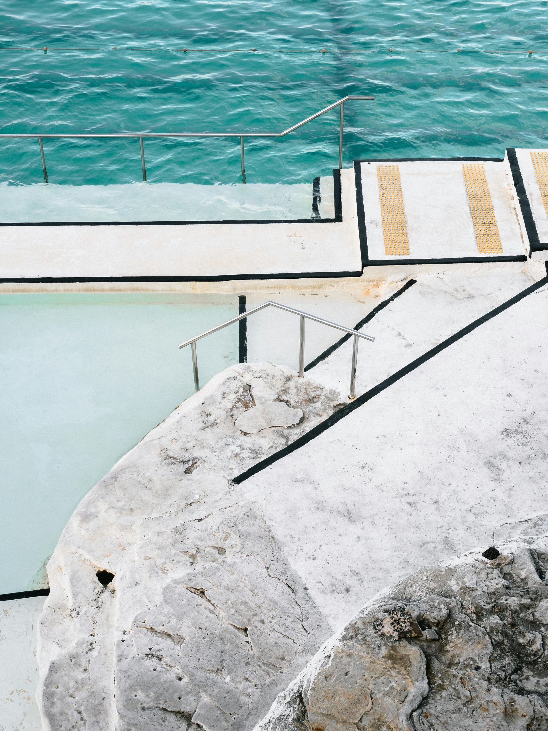 Luxury waterfront hardscape with white stone paving and metal railings over turquoise water