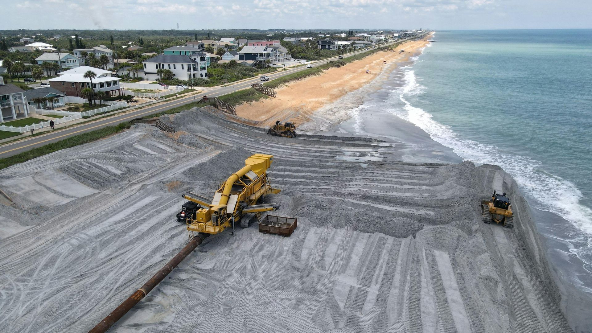 Heavy machinery installing coastal drainage infrastructure on Florida beach to protect nearby homes