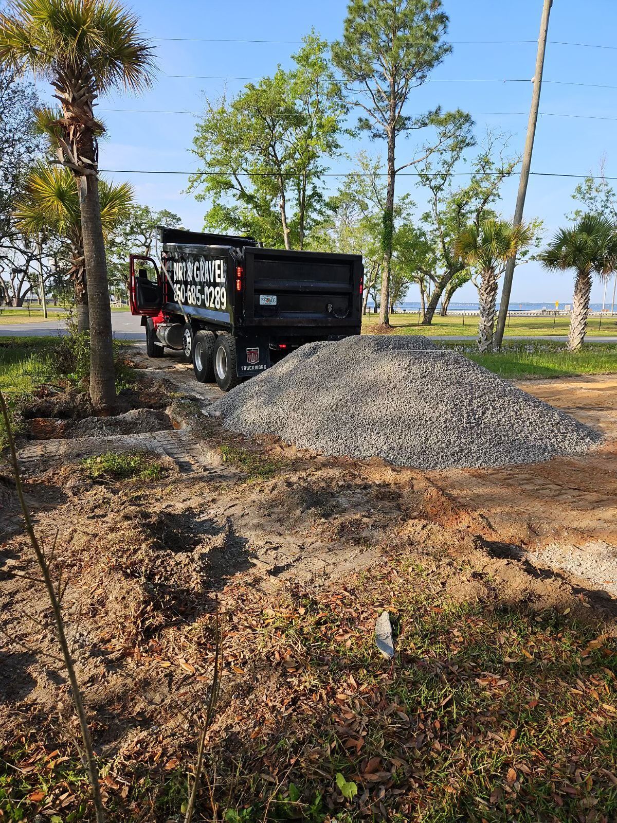 A dump truck is driving down a dirt road next to a pile of gravel.