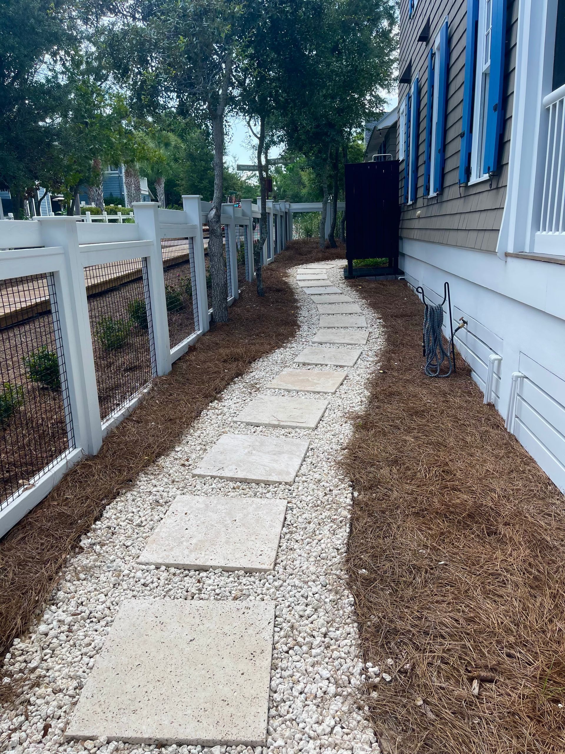 A walkway leading to a house with a white fence and blue shutters.