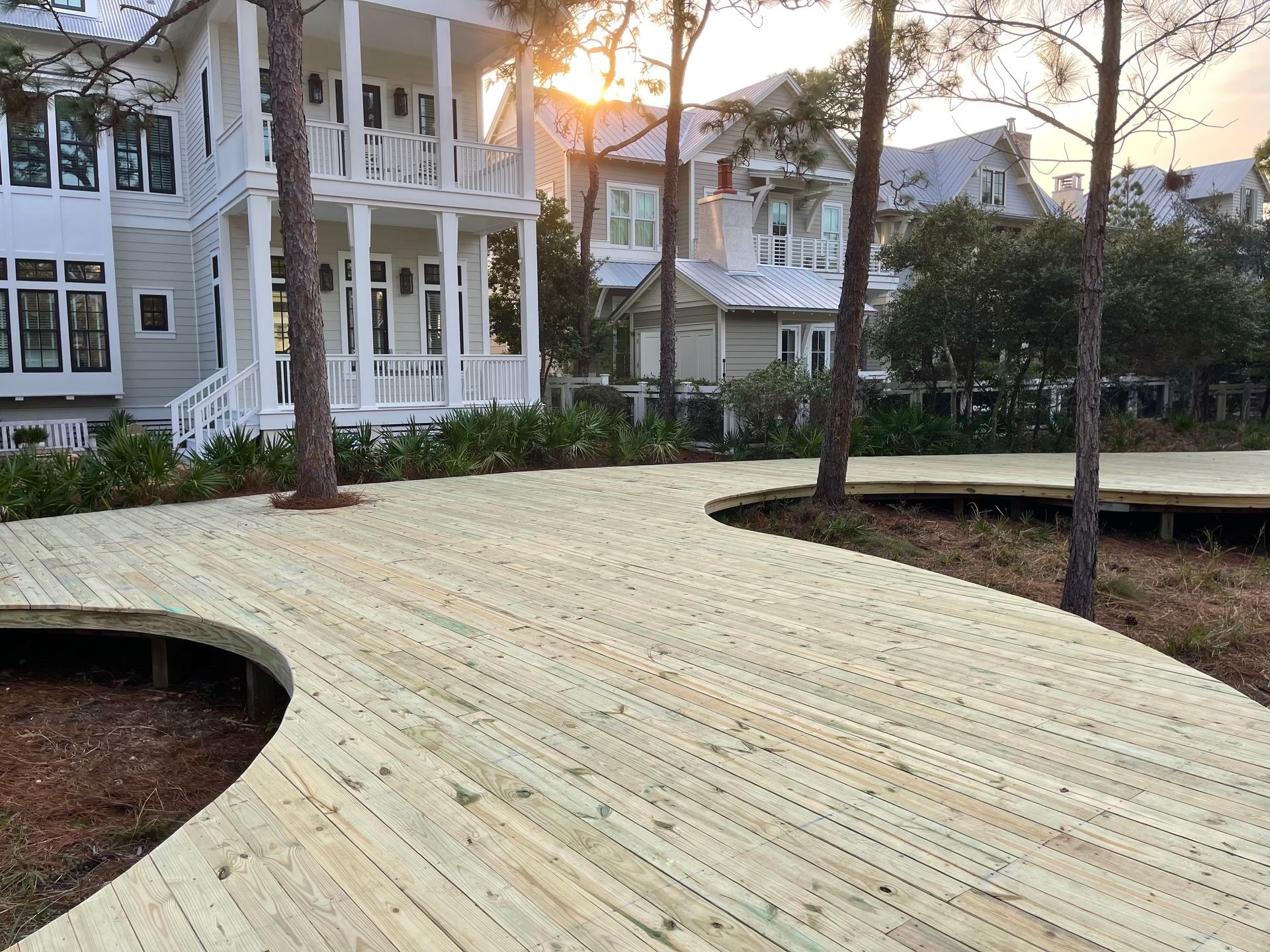 A wooden walkway leading to a white house surrounded by trees.
