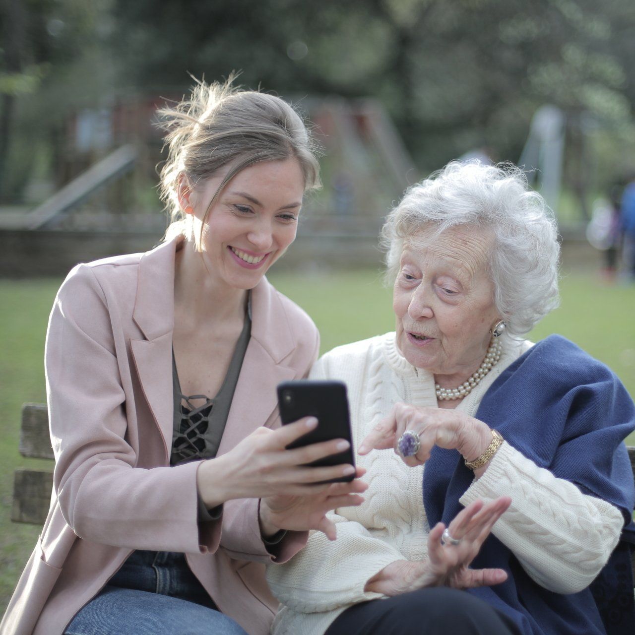 A young woman is showing an older woman how to use a cell phone.