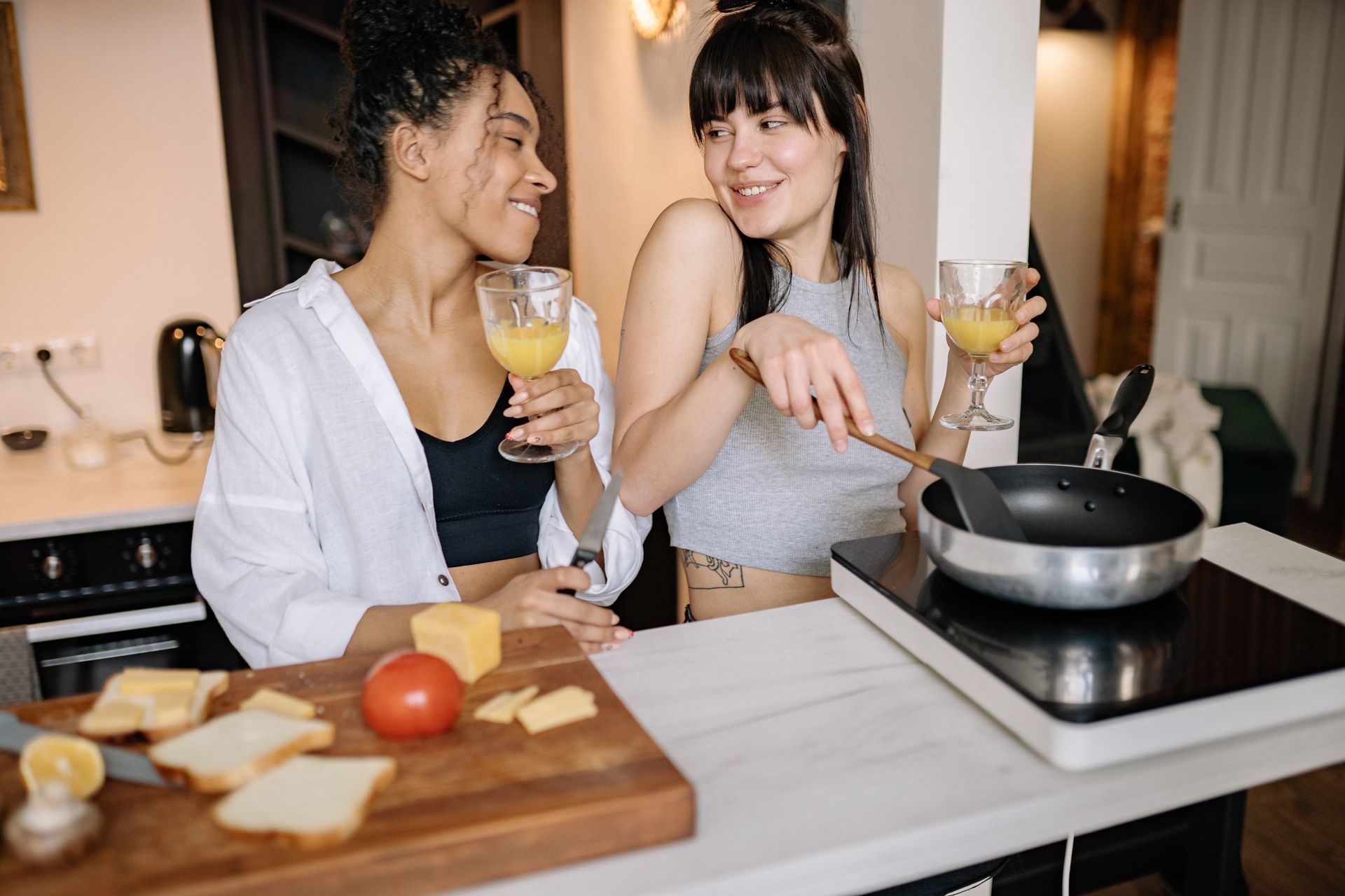 Two women are cooking together in a kitchen and drinking wine.