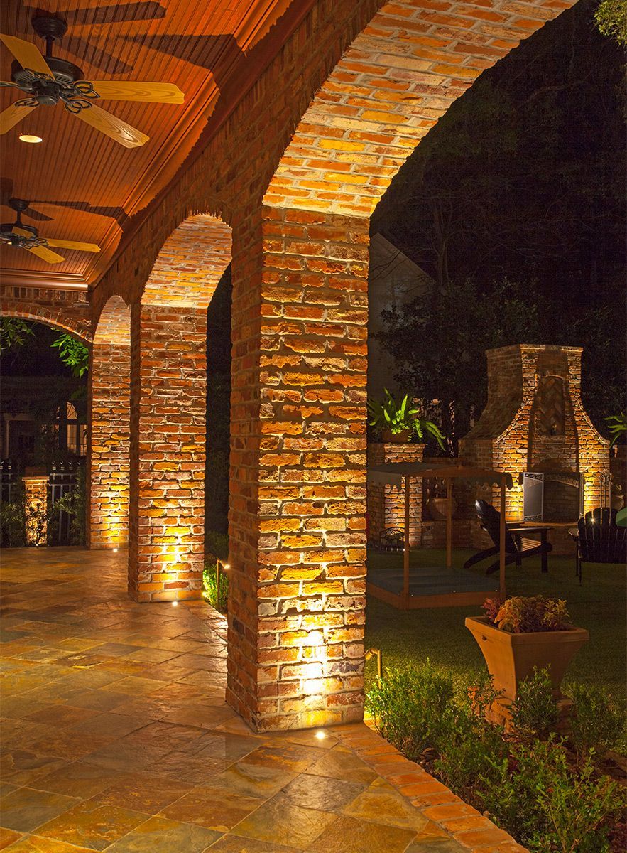 A patio with brick arches and a fireplace at night that is surrounded by bright lights.